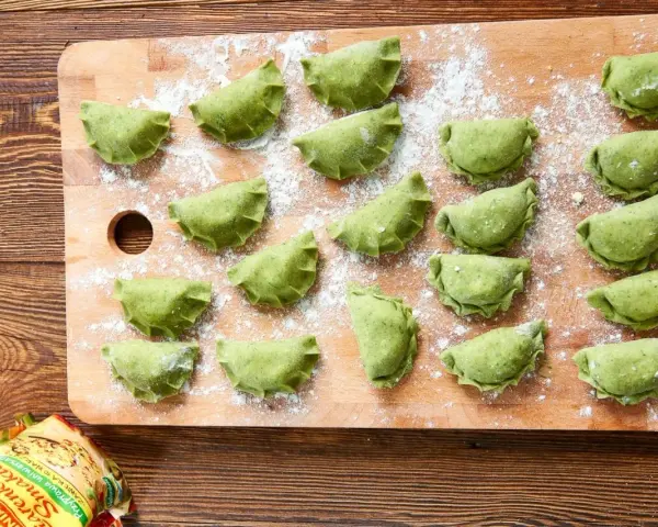 Zielone pierogi ze szpinakiem ułożone na desce, posypane mąką. Czekają na gotowanie.