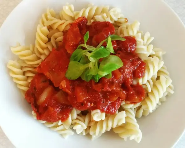 Fusilli z bogatym, domowym makaronem z sosem pomidorowym, udekorowane świeżymi listkami.