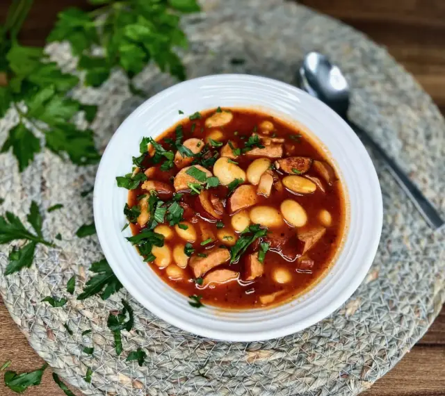 Aromaticzna fasolka po bretońsku z kiełbasą i fasolą, posypana świeżą natką pietruszki, czeka na talerzu.