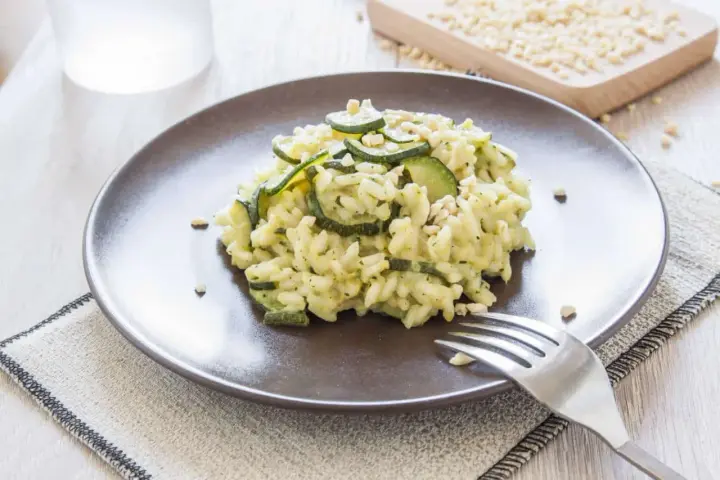 Kremowe risotto z cukinią i orzeszkami pinii, podane na brązowym talerzu.