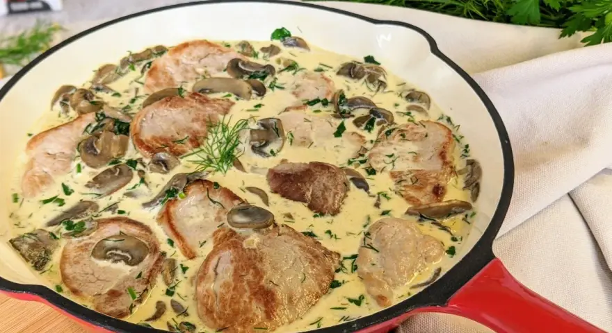Soczyste polędwiczki w kremowym sosie z pieczarkami i koperkiem, podane w czerwonej patelni. Pyszne danie gotowe do podania.