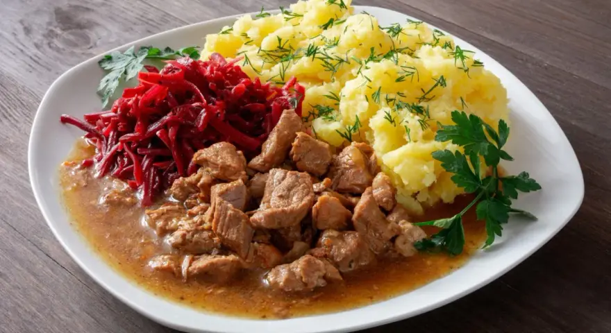 Pyszny gulasz z łopatki w sosie, podany z purée ziemniaczanym i surówką z buraczków.