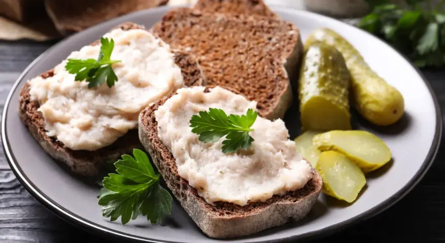 Domowy smalec przepis babci na ciemnym chlebie, ozdobiony natką pietruszki, z ogórkami kiszonymi. Pyszne, tradycyjne danie.