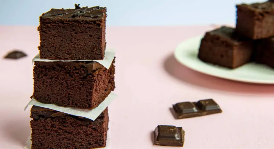 Ciemne, wilgotne brownie z fasoli, ułożone w wieżę, obok kawałków czekolady.