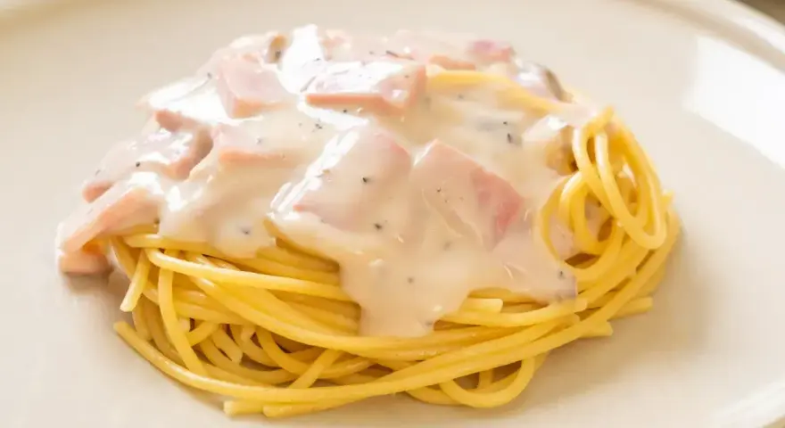 Pyszny makaron z serem i kawałkami szynki, polany kremowym sosem. Idealny na szybki obiad.