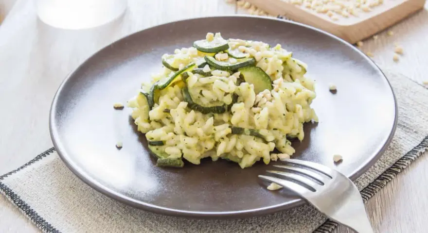 Kremowe risotto z cukinią i orzeszkami pinii, podane na brązowym talerzu.