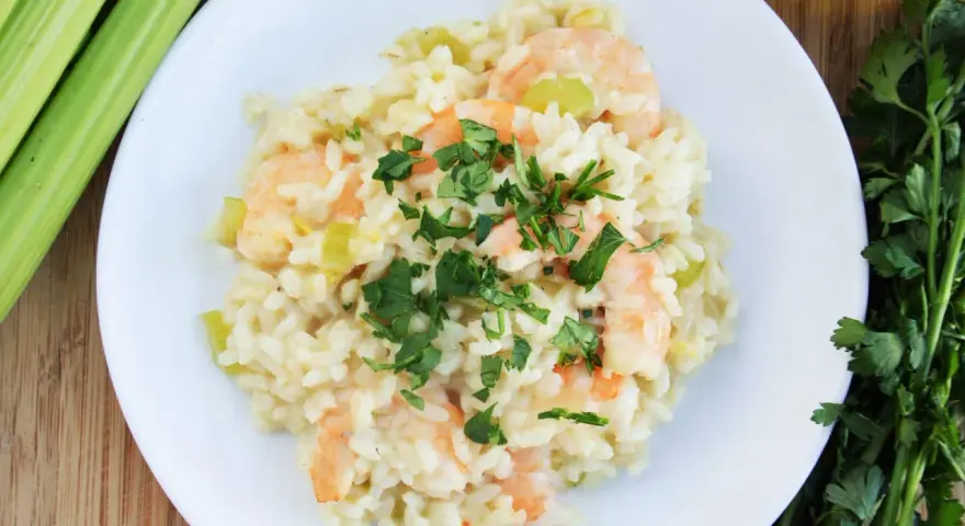 Pyszne risotto z krewetkami, udekorowane natką pietruszki, obok łodygi selera i oliwy.