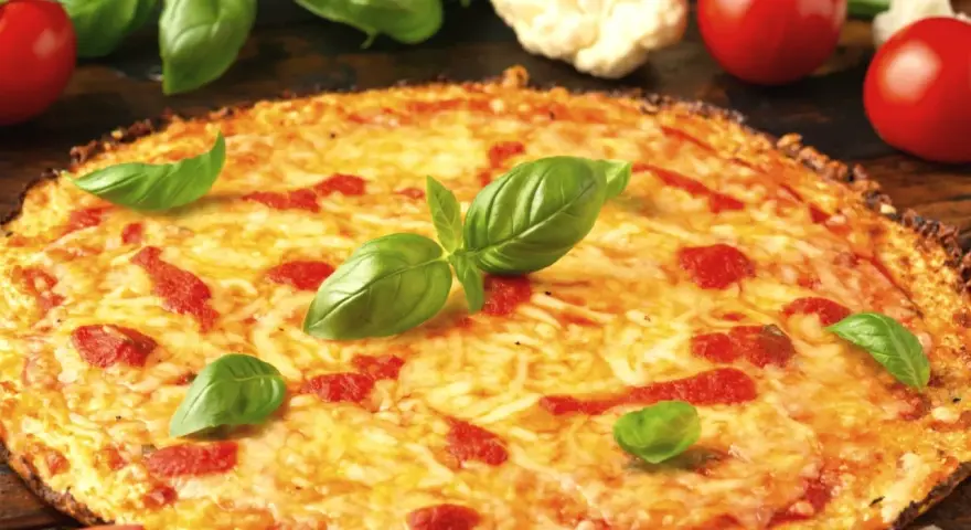 Pyszne ciasto na pizzę z serem, pomidorami i bazylią. Obok leżą świeże pomidory i kalafior.
