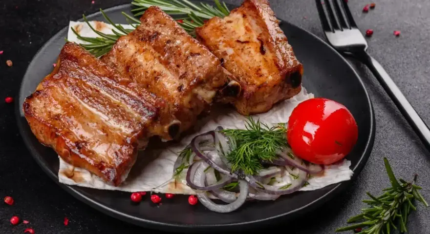 Soczyste, pieczone żeberka w rękawie, podane z pomidorkiem, cebulą i rozmarynem.
