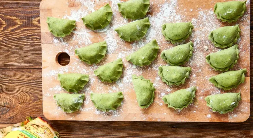 Zielone pierogi ze szpinakiem ułożone na desce, posypane mąką. Czekają na gotowanie.