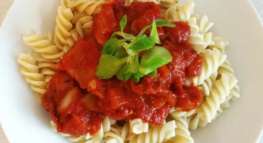 Fusilli z bogatym, domowym makaronem z sosem pomidorowym, udekorowane świeżymi listkami.
