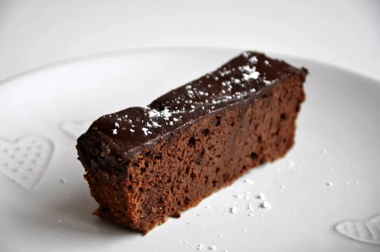 Wilgotny brownie z fasoli, polany czekoladą i posypany cukrem pudrem, na talerzu z serduszkami.