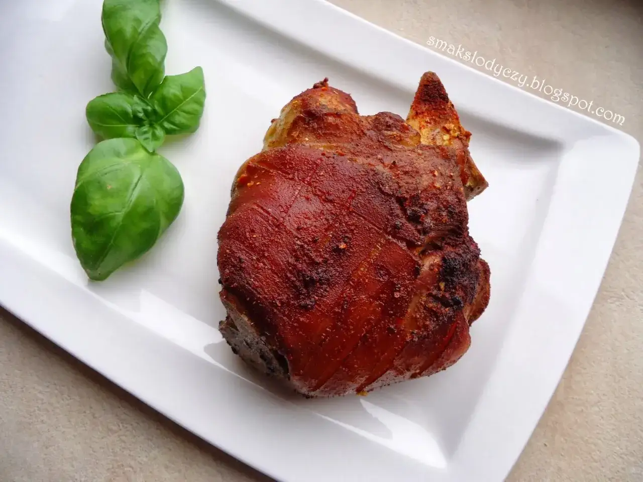 Apetyczna golonka w piwie, pieczona do perfekcji, podana z gałązką świeżej bazylii na białym talerzu.