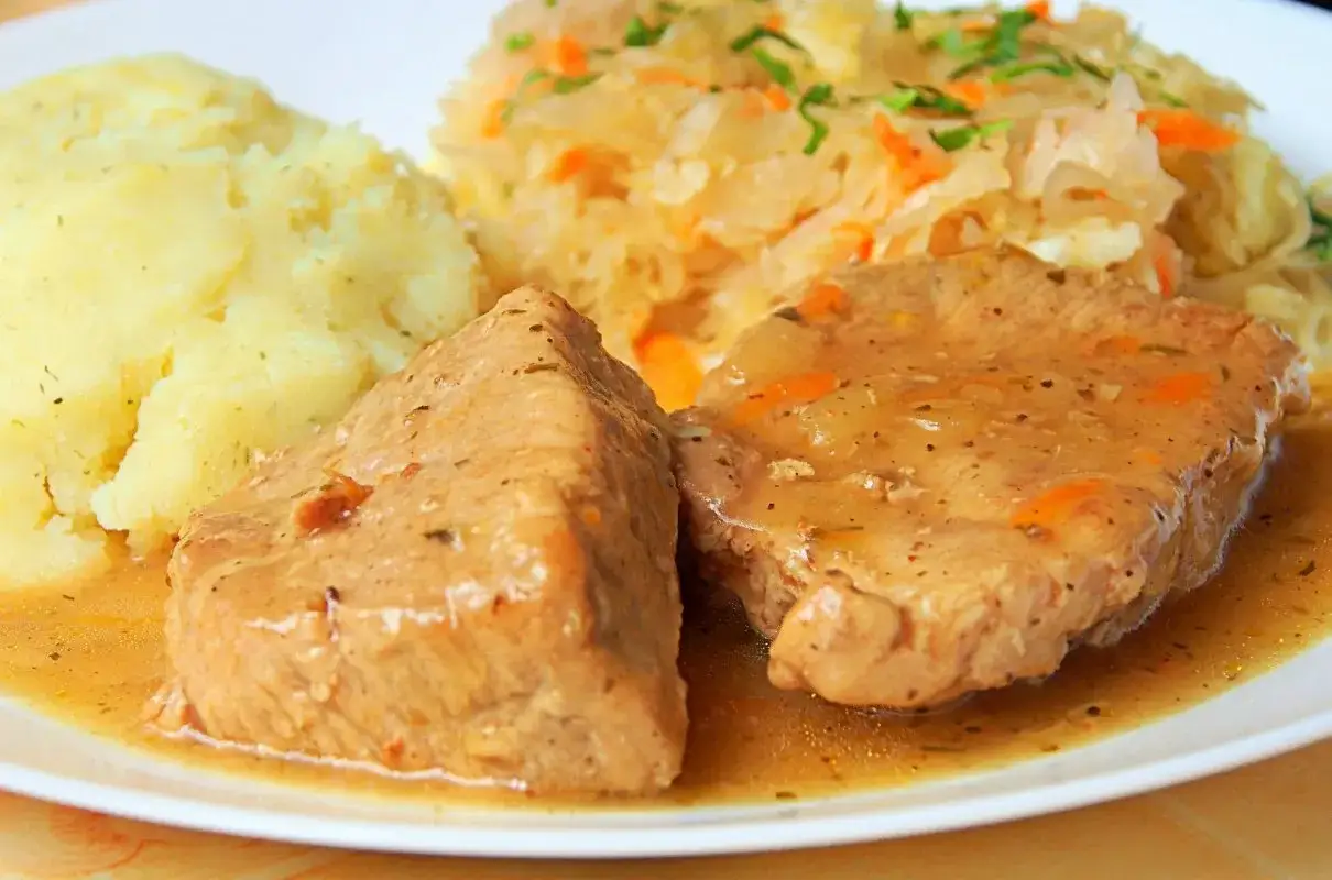 Dwa kawałki soczystej szynki w sosie własnym, podane z purée ziemniaczanym i surówką z kiszonej kapusty. Pyszny, domowy obiad.