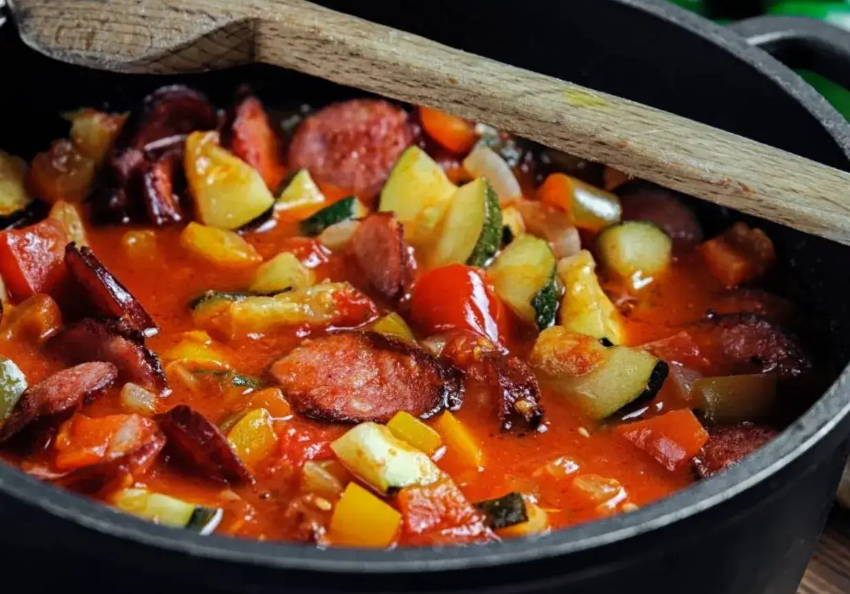 Gęste, aromatyczne leczo z pieczarkami, papryką i kiełbasą, gotujące się w garnku, z drewnianą łyżką.