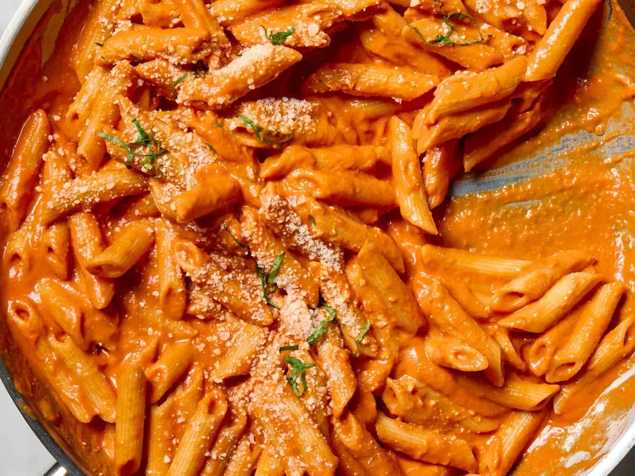 Penne alla vodka w kremowym sosie pomidorowym, posypane parmezanem i świeżą bazylią.