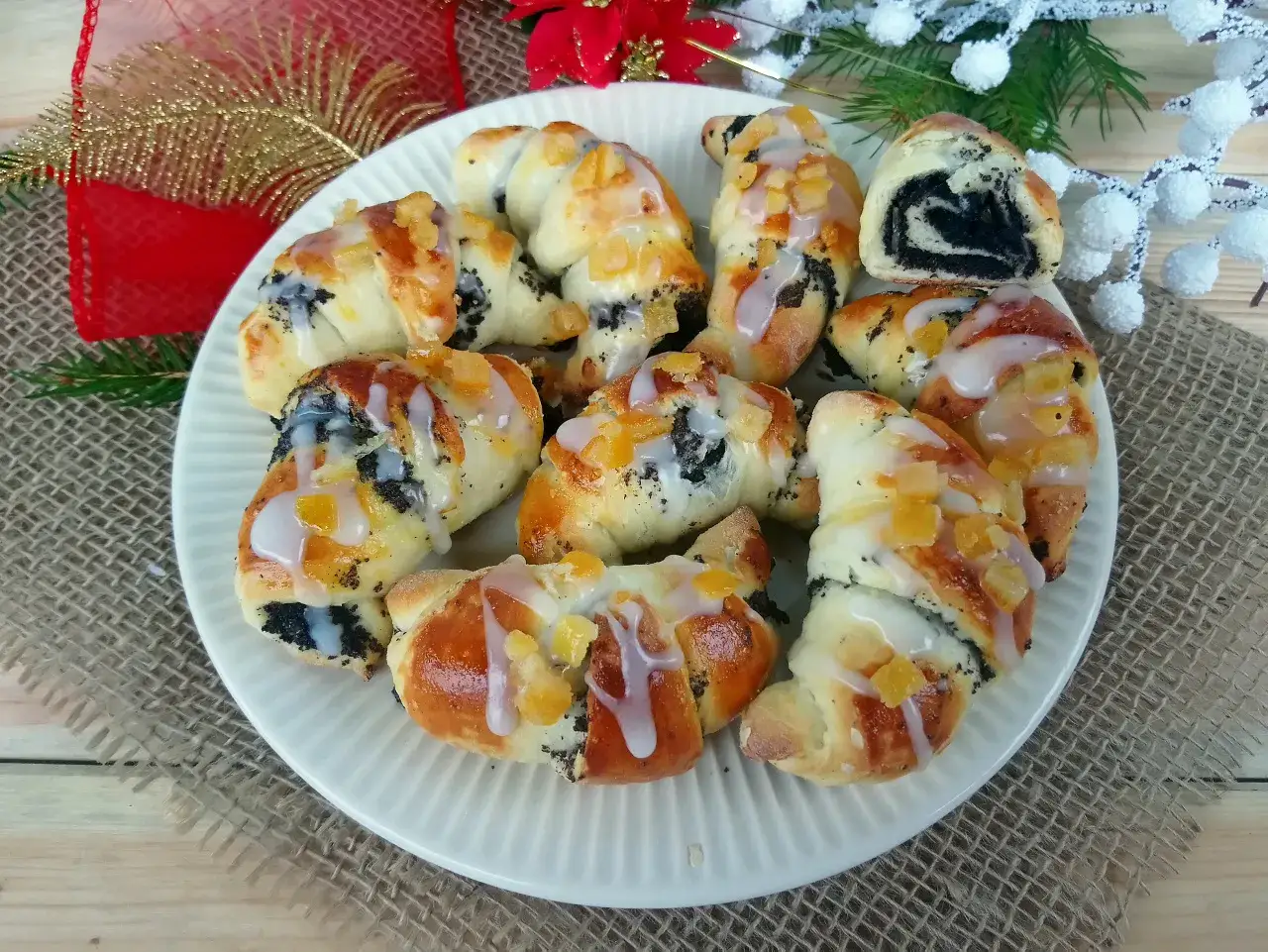Pyszne rogaliki z makiem, polane lukrem i posypane kandyzowanymi owocami, prezentują się apetycznie na talerzu.