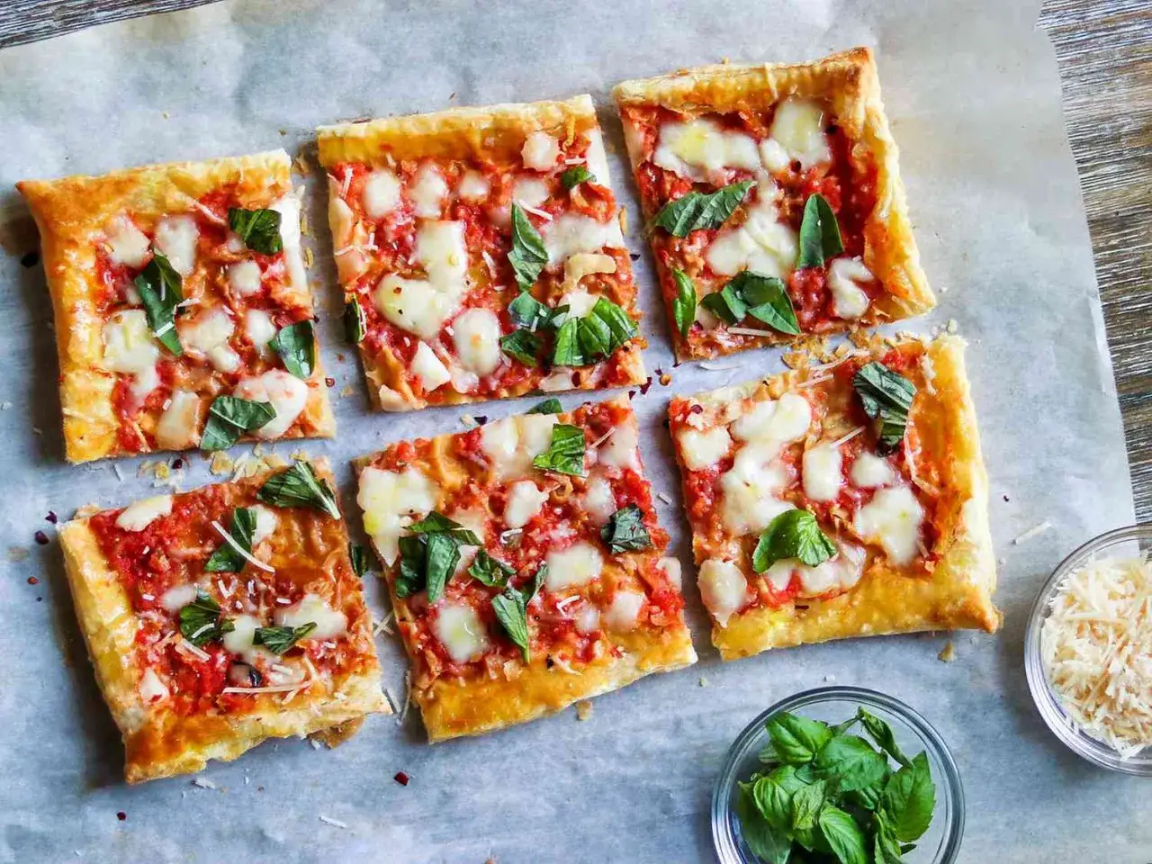 Sześć kwadratowych kawałk&oacute;w pysznej pizzy z ciasta francuskiego, z pomidorami, mozzarellą i bazylią.