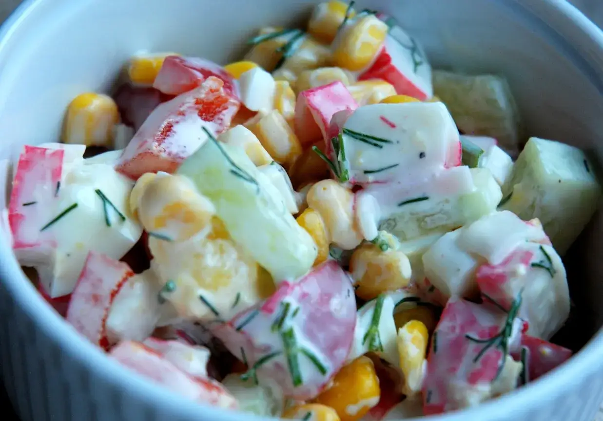 Pyszna sałatka z surimi, kukurydzy, jajek i ogórka, doprawiona koperkiem.