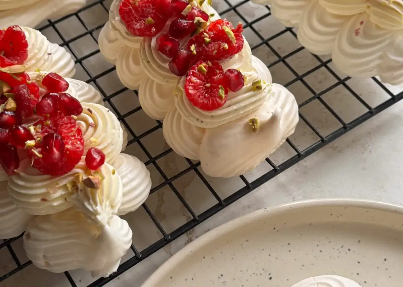 Mini bezy pavlova z malinami i granatem, posypane pistacjami, wyglądają apetycznie.