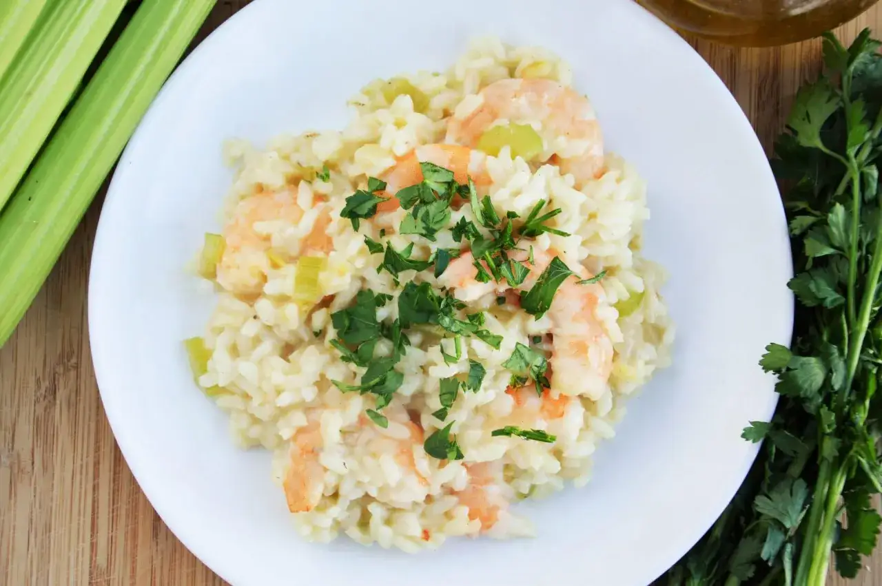 Pyszne risotto z krewetkami, udekorowane natką pietruszki, obok łodygi selera i oliwy.