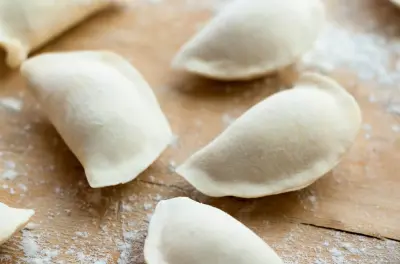Surowe ciasto na pierogi uformowane w kształt półksiężyca, rozsypane na drewnianej desce.