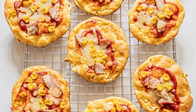 Mini pizze z serka wiejskiego, z kukurydzą i kawałkami mięsa, ułożone na metalowej kratce.