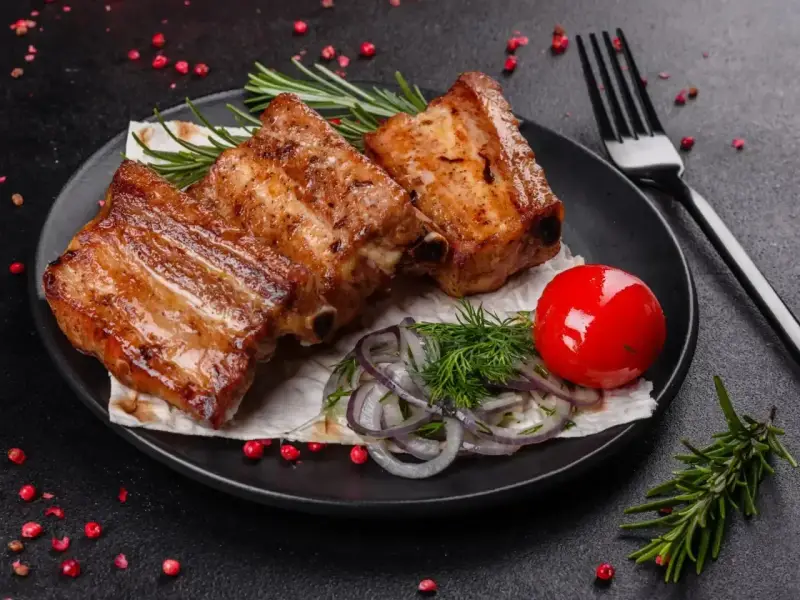 Soczyste, pieczone żeberka w rękawie, podane z pomidorkiem, cebulą i rozmarynem.